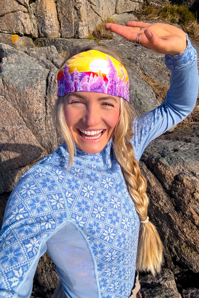A smiling blond woman wearing the Snowy Path headband in front of rocks